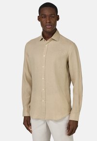 Camicia beige a maniche lunghe realizzata in tessuto leggero, con chiusura a bottoni, colletto a punta e orlo arrotondato. Finitura texturizzata, design semplice.
