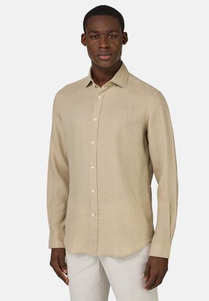 Camicia beige a maniche lunghe realizzata in tessuto leggero, con chiusura a bottoni, colletto a punta e orlo arrotondato. Finitura texturizzata, design semplice.