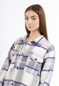 Camicia a scacchi viola e grigia realizzata in tessuto morbido, con due tasche sul petto, colletto e bottoni marroni.