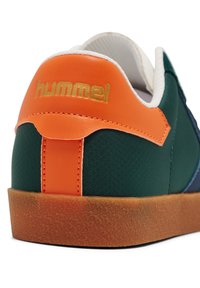 Grüne und blaue Sneaker mit orangefarbenen Akzenten, strukturiertem Stoff, Gummisohle und einem goldenen "hummel"-Logo an der Ferse.