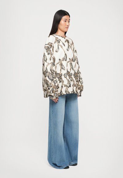 Long-sleeve cream sweatshirt with black and gold floral embroidery, paired with wide-leg light blue jeans and black shoes.