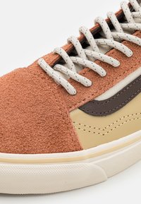 Hnědé semišové tenisky s béžovými koženými detaily, bavlněnými tkaničkami a texturovanou gumovou podešví. Obsahují kontrastní švy a klasický design.