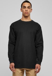 Langermet svart bomulls t-skjorte med rund hals, med en avslappet passform og rette mansjetter, vist på en modell mot en grå bakgrunn.