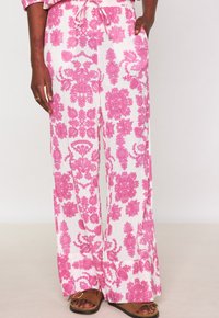 Pantalon blanc avec un motif floral rose, doté d'une taille à cordon, d'un design à jambes larges et de poches latérales. Tissu léger texturé.