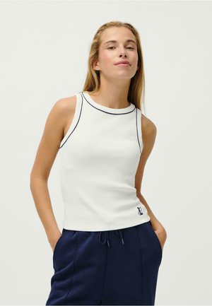 Top senza maniche bianco a costine con scollatura rotonda, caratterizzato da piping blu contrastante e un piccolo logo all'orlo. Abbinato a pantaloni blu.