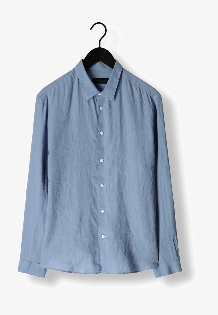 Lyseblå langærmet skjorte med knapper og krave hængende på en sort bøjle mod en hvid baggrund.