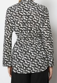 Blusa a maniche lunghe con un motivo geometrico bianco e nero, dotata di una vita con cintura, colletto e polsini con bottoni. Tessuto dalla texture liscia.