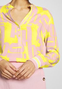 Camisa de manga larga con botones que presenta un atrevido patrón gráfico en amarillo y rosa, con un ligero cuello y puños a rayas.