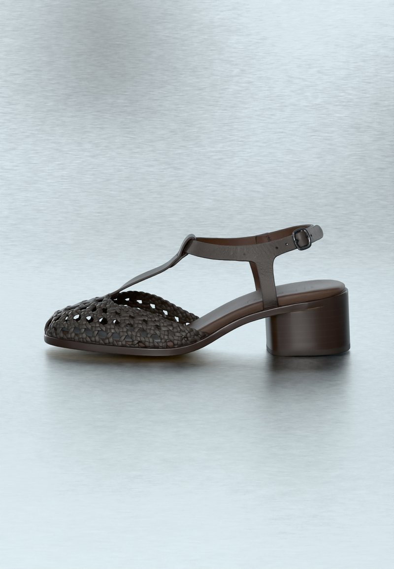 Brown leather low-heeled sandal with woven toe design, ankle strap, and buckle on a smooth light gray background.