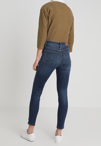 Dark blue skinny jeans with a high waist, back pockets, and a leather patch at the waistband, paired with a brown cropped sweater.