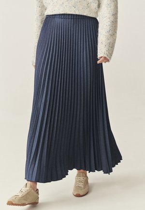 Jupe maxi plissée bleu marine en tissu texturé, dotée d'une taille haute et d'un design fluide, associée à des baskets beige clair.