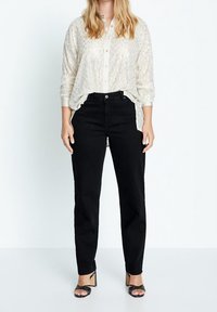 Zwarte jeans met een hoge taille, gecombineerd met een getextureerd, crème-kleurig overhemd met knopen, voorzien van een subtiele glans en opgerolde mouwen.