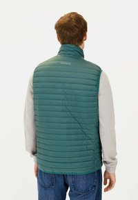 Grüne gepolsterte Weste mit hohem Kragen, mit horizontaler Stepptextur und Reißverschlussakzenten. Getragen über einem grauen Langarmshirt.