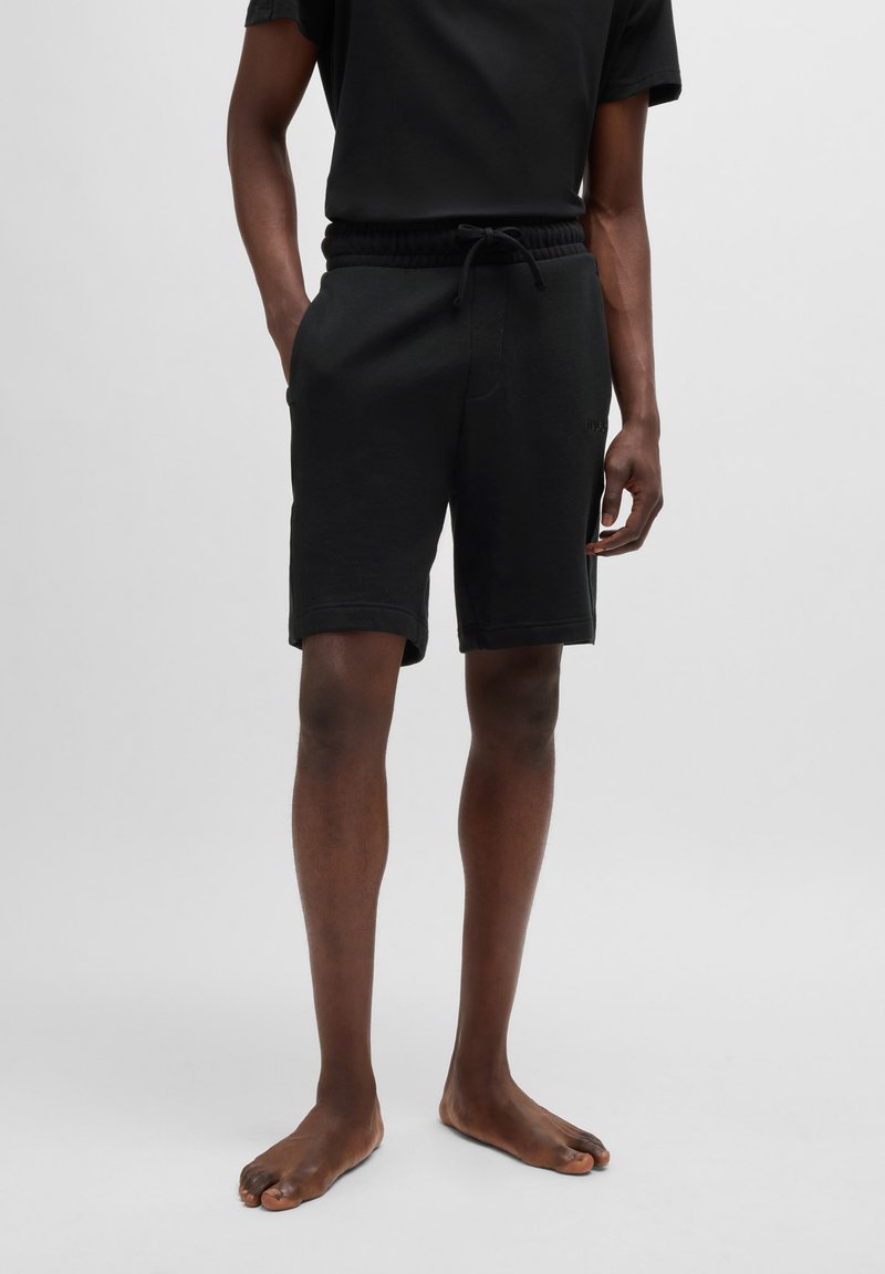 Mustat puuvillashortsit, joissa on joustava vyötärö ja kiristysnauha, sivutaskut sekä hieman rento leikkaus. Sujuva pinta ja polven pituus.