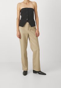 Top nero senza spalline con un design aderente e bottoni al centro, abbinato a pantaloni beigi a vita alta e scarpe nere a punta.