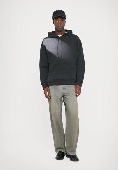 Črna kapuco siva potiskanih motiov, kenguru žep; nosi se z svetlo sivo naravnost krojenimi kavbojkami in črnimi čevlji. Črna kapa.