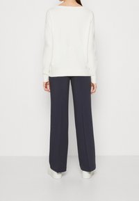 Pull blanc à manches longues associé à un pantalon large marine et des baskets blanches, avec une coupe décontractée et des poignets côtelés.