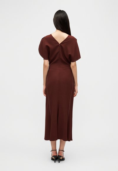 Μίντι φόρεμα μπορντό με V-πλάτη, κοντά φουσκωτά μανίκια και αντίθετη ραφή. Κατασκευασμένο από απαλό ύφασμα, με ρέουσα σιλουέτα, συνδυασμένο με μαύρες πέδιλες με λουράκια.