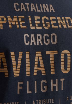Marineblå stof t-shirt med stort, fedt, guldfarvet tekst, der har forskellige luftfartsrelaterede ord og sætninger trykt i forskellige størrelser og stilarter.