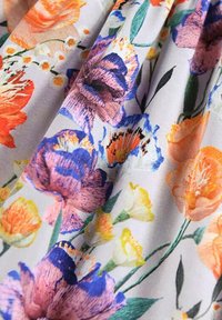 Blommönstrad tyg med stora orange, lila och gula blommor på en ljusgrå bakgrund, med gröna blad som visar fint mönster och livfulla färger.
