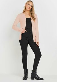 Cardigan rosa chiaro con scollo rotondo e chiusura a bottoni, abbinato a una canotta nera e jeans fitted neri. Stivaletti neri alla caviglia completano il look.