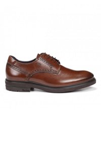 Zapato de vestir de cuero marrón con un acabado suave, perforaciones decorativas y una suela negra resistente. Logo de la marca visible en el lateral.