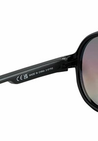 Lunettes de soleil en plastique noir avec des verres sombres. La branche présente un texte en relief : "CE UK CA FABRIQUÉ EN CHINE 3-6 ANS." Texture lisse. Forme ronde.