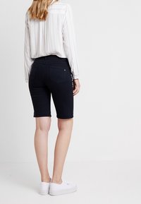 Tmavě modré bermudy, délka do poloviny stehna, se dvěma zadními kapsami. V kombinaci s bílou košili s pruhy a bílými teniskami.