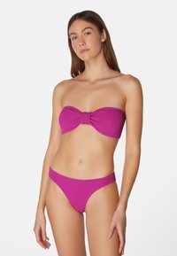 Rosa, stickad bandeau-bikini med en rosett detalj på toppen och matchande låghöga bottnar. Texturerad tyg med minimala accent.
