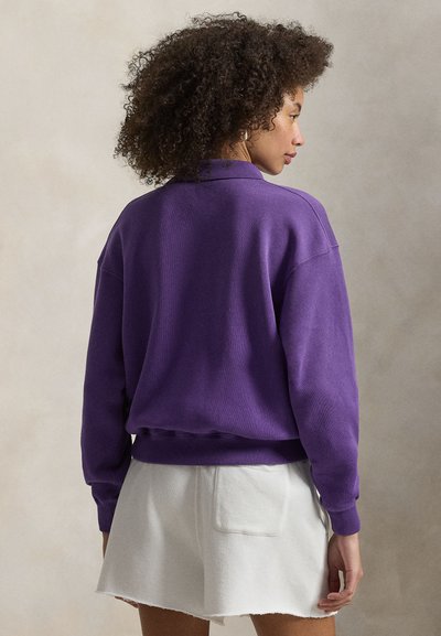 Μωβ φαρδιά φούτερ με ψηλό λαιμό και ριμπ μανσέτες, σε συνδυασμό με λευκή, ελαφρώς ξεφτισμένη φούστα-σορτς με τσέπη πατς.