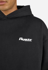 Black hoodie made of soft fabric featuring a white "Pegador" logo on the chest, with a drawstring hood and ribbed cuffs.