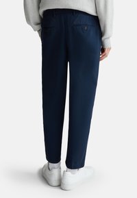 Marineblauwe chinos van lichtgewicht stof, met twee achterzakken met knopen, slank model en contrasterende witte sneakers.