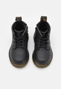 Bottines en cuir noir avec des surpiqûres jaunes, design à lacets, texture lisse et une sangle en boucle à l'arrière pour un enfilage facile.