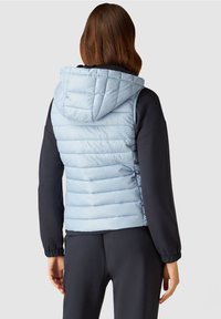 Ljusblå quiltad väst med huva, med horisontell sömnad. Parat med en mörk långärmad topp och slanka svarta byxor.