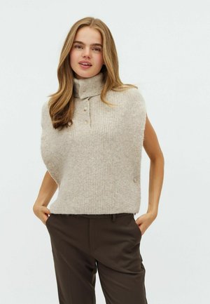 Beżowy sweter bez rękawów z dzianiny z wysokim kołnierzem, ozdobiony trzema guzikami przy szyi i miękką fakturą, w zestawie z ciemnymi spodniami.
