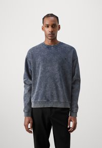 Mørkeblå crewneck genser i mykt, teksturert stoff, med en falmet vask og ribbestrikkede mansjetter og nederkant. Liten logo på brystet.
