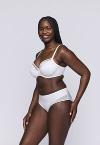 Biały stanik i zestaw majtek o wysokim stanie z przezroczystymi wstawkami i pionowym prążkowanym wzorem. Miseczki są lekko uformowane dla wsparcia.