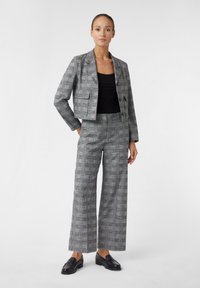 Costume gris à carreaux comprenant un blazer court et un pantalon large. Tissu lisse avec une texture subtile, assorti d'un haut noir et de mocassins.