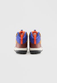 Egy színes sneakerpár, kék steppelt szövettel, narancssárga húzópántokkal, barna sarkpanelokkal, fehér középtalppal és fekete textúrált talppal, hátulról nézve.