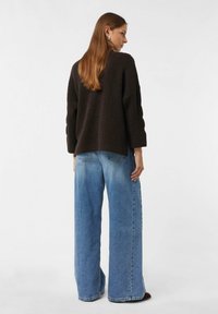 Maglione a maglia strutturata di colore marrone scuro, con maniche a tre quarti, abbinato a jeans a gamba larga a vita alta in denim di colore blu chiaro.