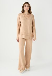 Set loungewear beige in maglia composto da un top a maniche lunghe con scollatura a V e pantaloni a gamba larga con orlo a coste, realizzato in un morbido tessuto testurizzato.