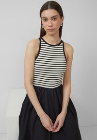 Gestreifter ärmelloser Top in Creme und Schwarz, kombiniert mit einem lockeren schwarzen Rock. Baumwollmischgewebe, das eine geraffte Taille und eine glatte Textur aufweist.