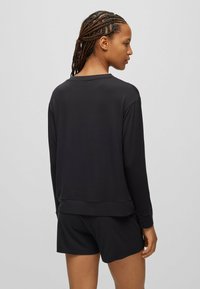 Zwarte lange mouwen top van zachte stof met een ronde hals, een iets cropped zoom en een relaxte pasvorm, gecombineerd met bijpassende zwarte shorts.