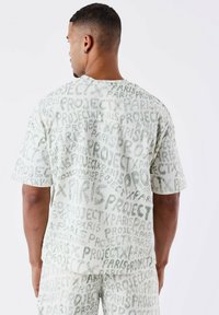 Camisa de manga corta, de color verde claro con un estampado, que lleva el texto "PROJECT PARIS" en tonos variados, con un corte relajado y tela suave y ligera.