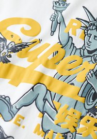 Tela blanca con un diseño gráfico de la Estatua de la Libertad en color verde azulado y un texto amarillo superpuesto. Incluye un águila con las alas extendidas.