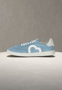 Ανοιχτό μπλε σουέτ αθλητικό παπούτσι με λευκά κορδόνια, λευκή σόλα και λευκό σχέδιο σε σχήμα καρδιάς στο πλάι, παρουσιάζεται σε ουδέτερο φόντο.