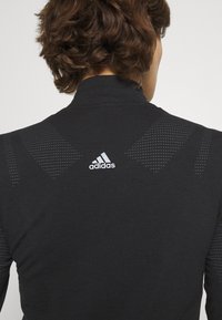 Black long-sleeve athletic top with high collar, featuring textured shoulder accents and white Adidas logo on the back.