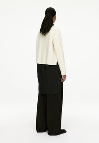 Cremfarbener, kurzer Pullover mit gerippten Bündchen und Saum, kombiniert mit einem schwarzen, langen, geschichteten Kleidungsstück. Glatte Textur, lockere Passform.