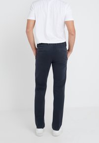Navy cotton chinos with a slim fit, featuring back pockets and a clean waistband, paired with a plain white short-sleeve shirt.