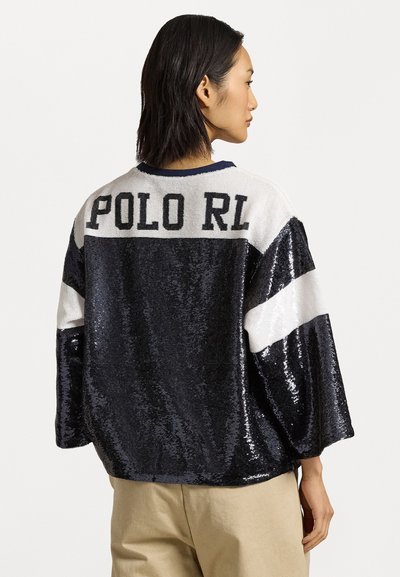 Sequined pullover in black and white, featuring "POLO RL" logo, loose-fit silhouette, drop sleeves, and ribbed neckline.
